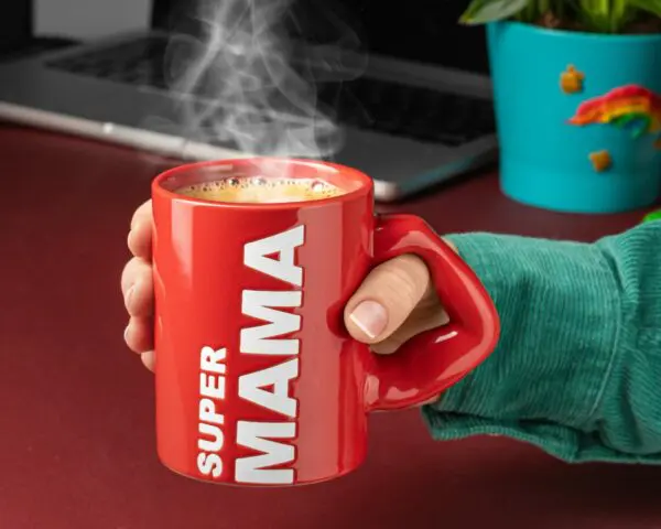 Czerwony kubek „Super Mama” stojący na biurku z gorącym napojem